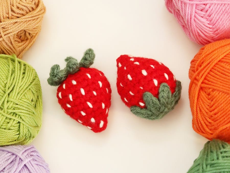 Palm-sized strawberry crochet project with textured embroidered seeds and leafy green topper.