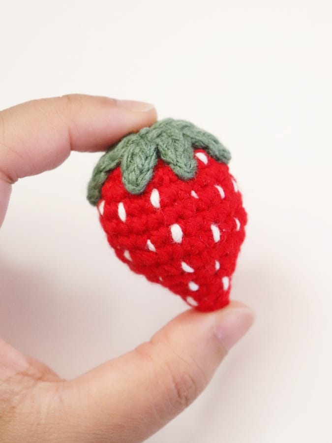Red amigurumi strawberry with embroidered details and green leaves, designed as a bag charm.